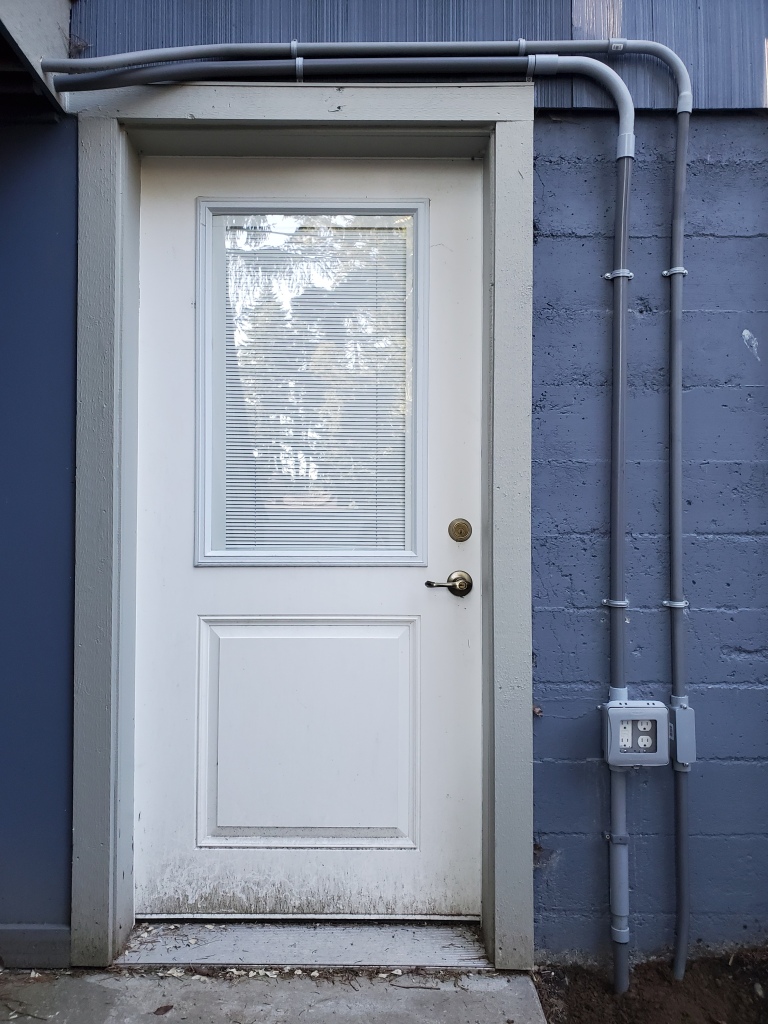 white door on blue exterior wall, with grey pvc conduit above and to the right of the door