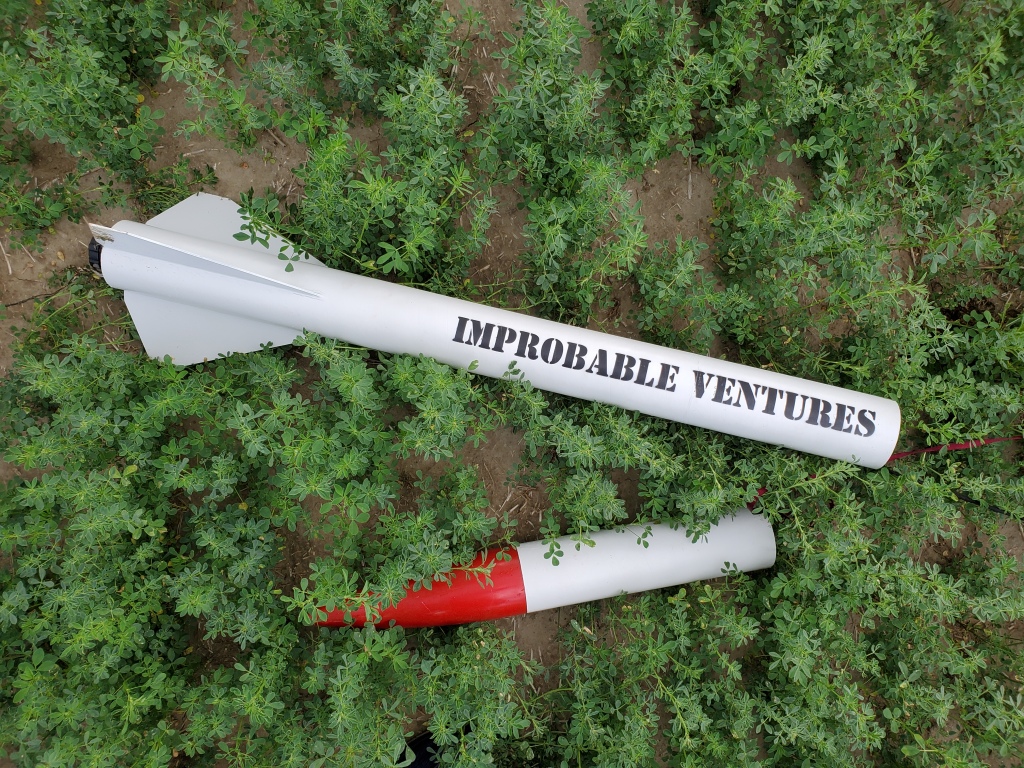 white rocket with text "improbable ventures" lying on ground in green field
